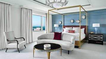 A modern hotel room with a four-poster bed, a round coffee table, a white sofa, and a view of the city.
