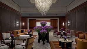 A spacious lobby with a grand chandelier, comfortable seating areas, and decorative vases with purple flowers.