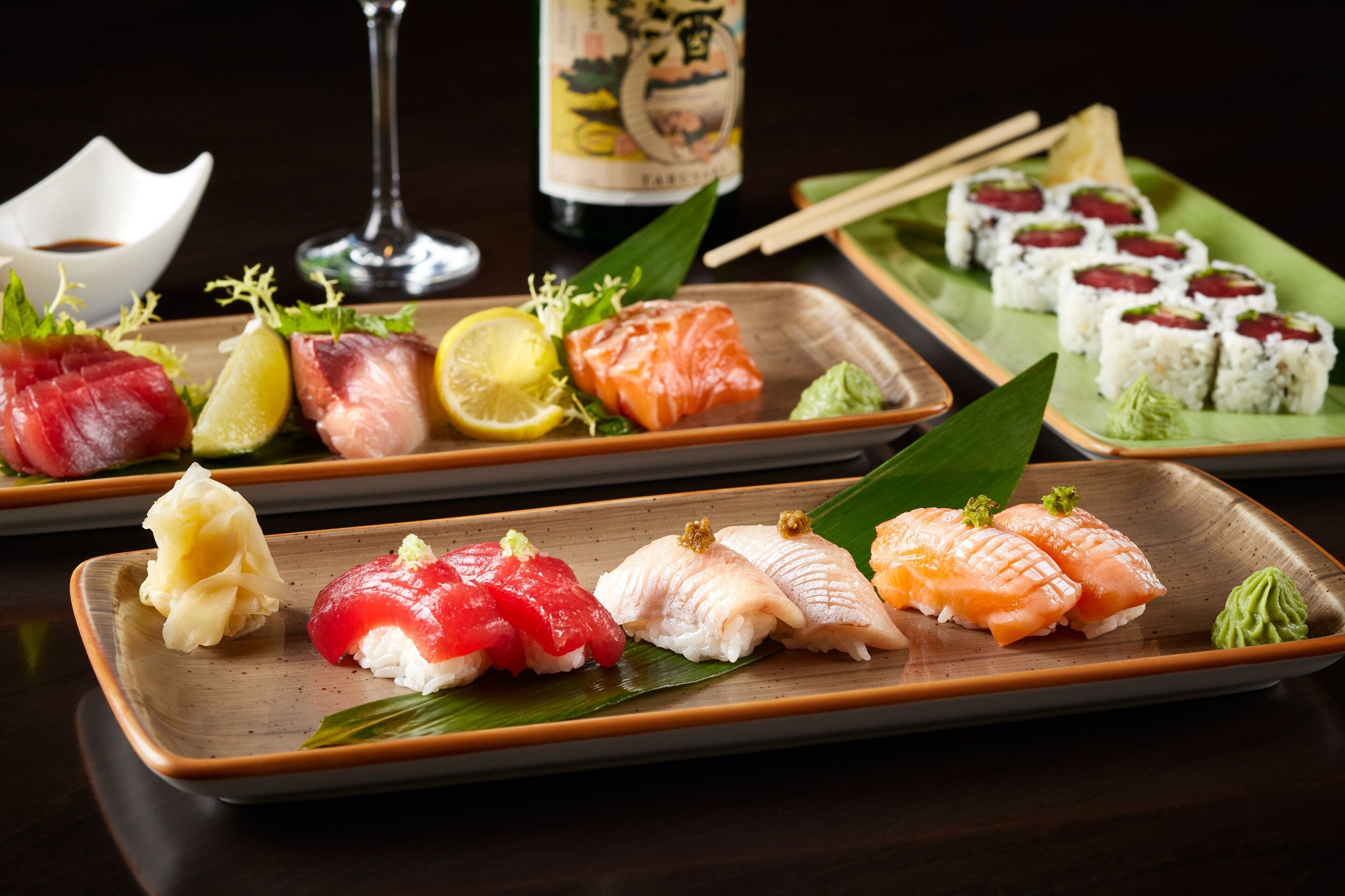 Variedad de platos de sushi en rectangular, con una botella y palillos de madera al fondo.