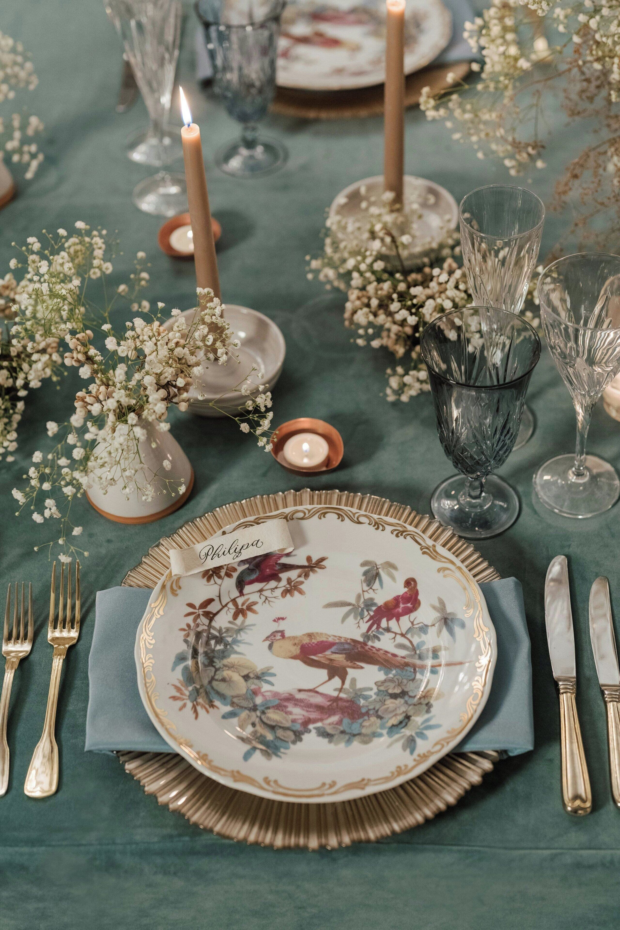 A table set with a floral plate, candles, and glassware, suggesting a formal dining arrangement.