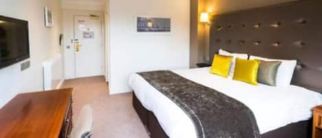 A hotel room with a large bed, a desk, a television, and a picture on the wall.