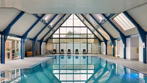Una piscina interior con un techo alto en arco y ventanas amplias.