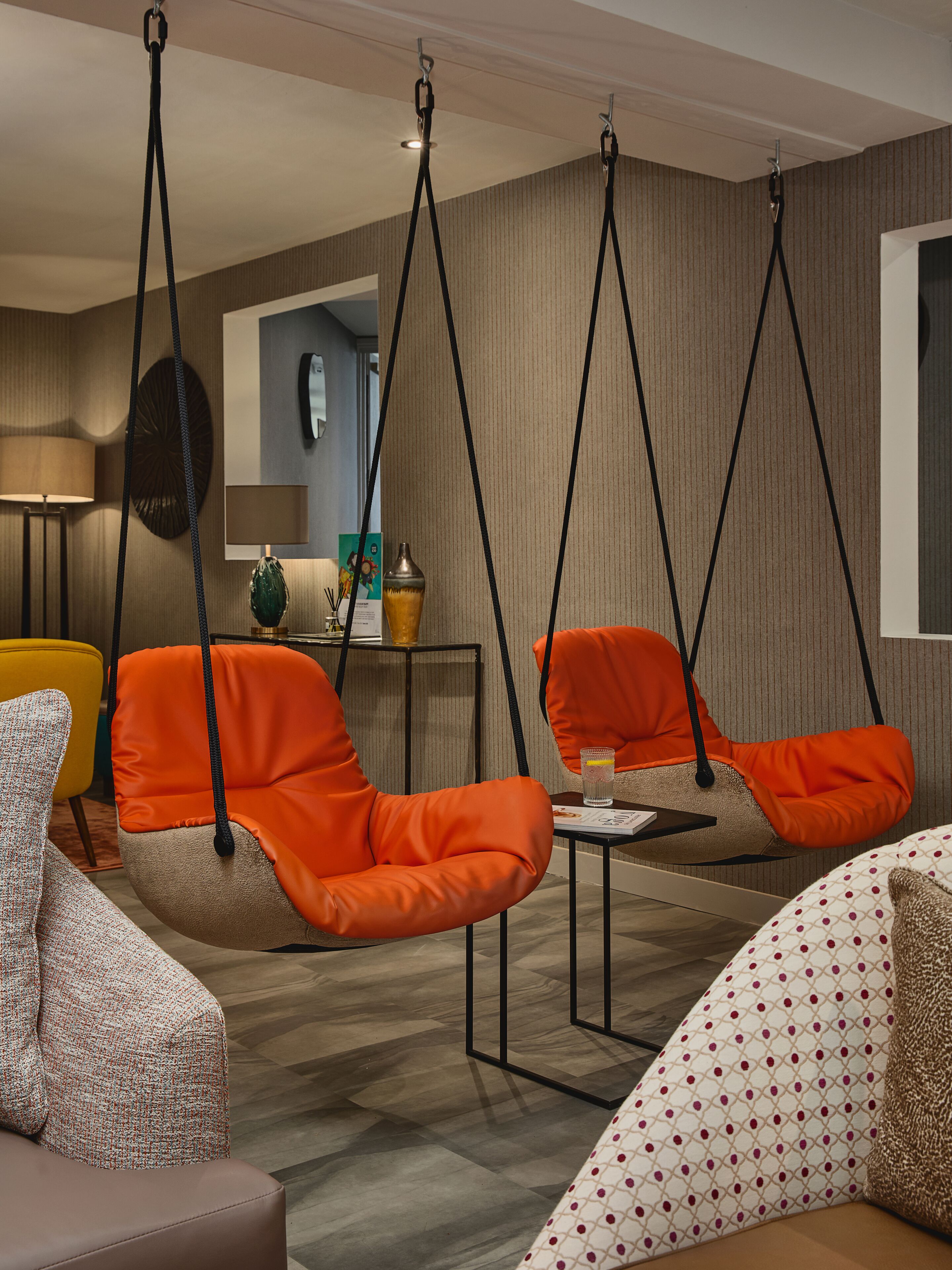 A modern living room with orange hanging chairs, a small table, and a patterned sofa.