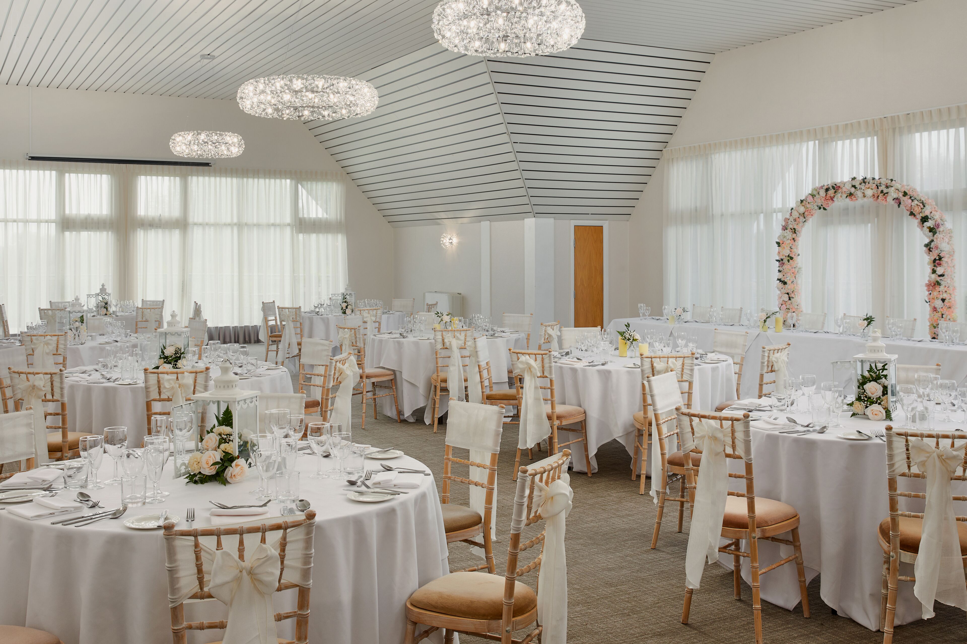 A banquet hall with round tables, white tablecloths, and floral centerpieces.
