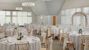 A banquet hall with round tables, white tablecloths, and floral centerpieces.