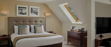 A bedroom with a large bed, a desk, a chair, a TV, and a skylight.