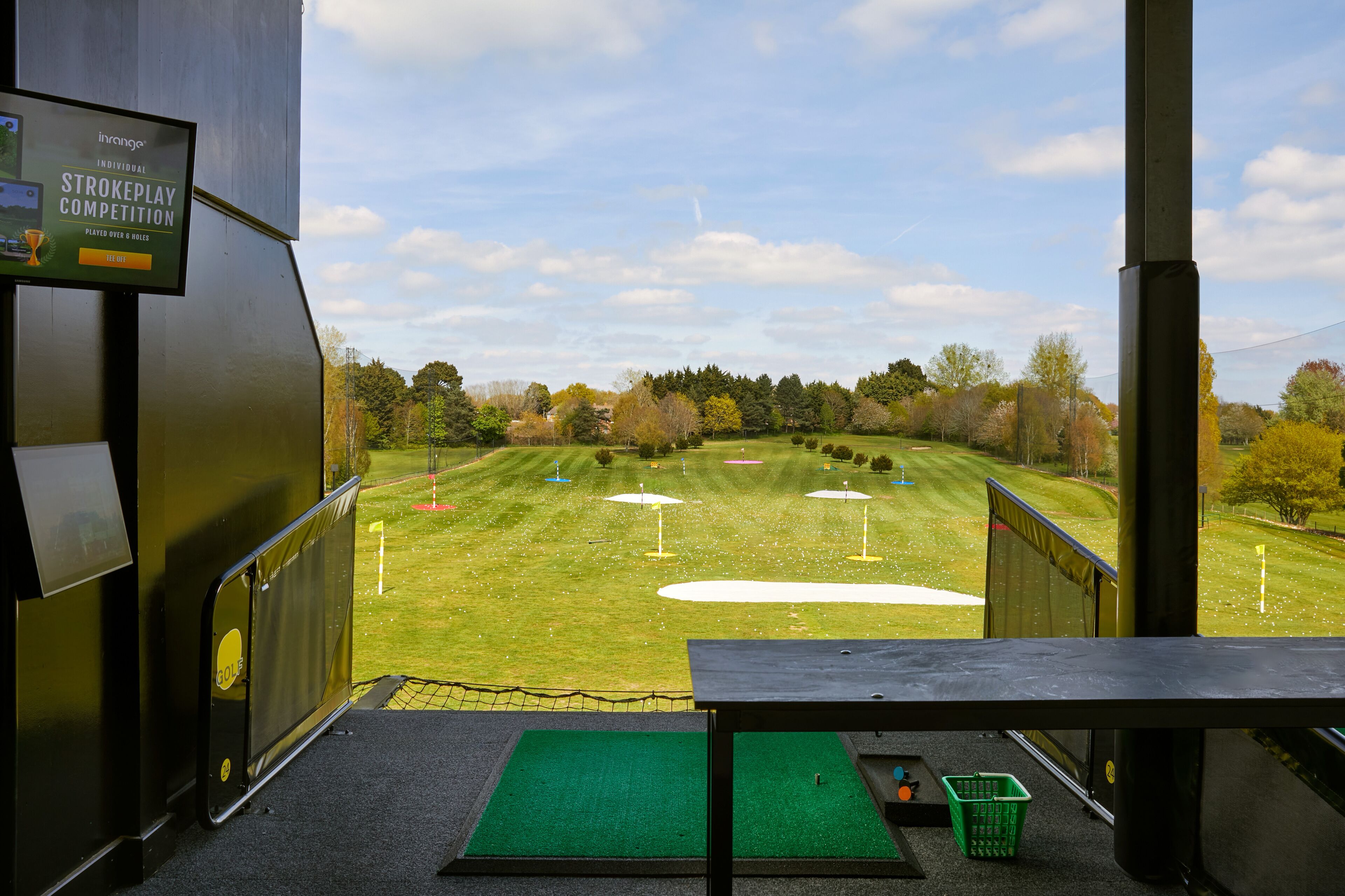 En golfbana med en utsiktsplattform, en skärm som visar resultaten från en slagspels tävling och en grön matta vid plattformens fot.