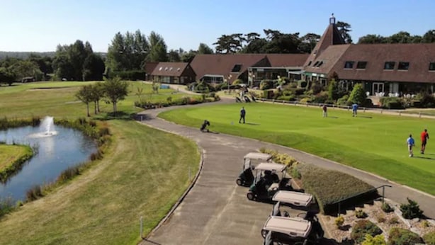 Un campo de golf con un estanque, carritos de golf y un edificio de techo inclinado.