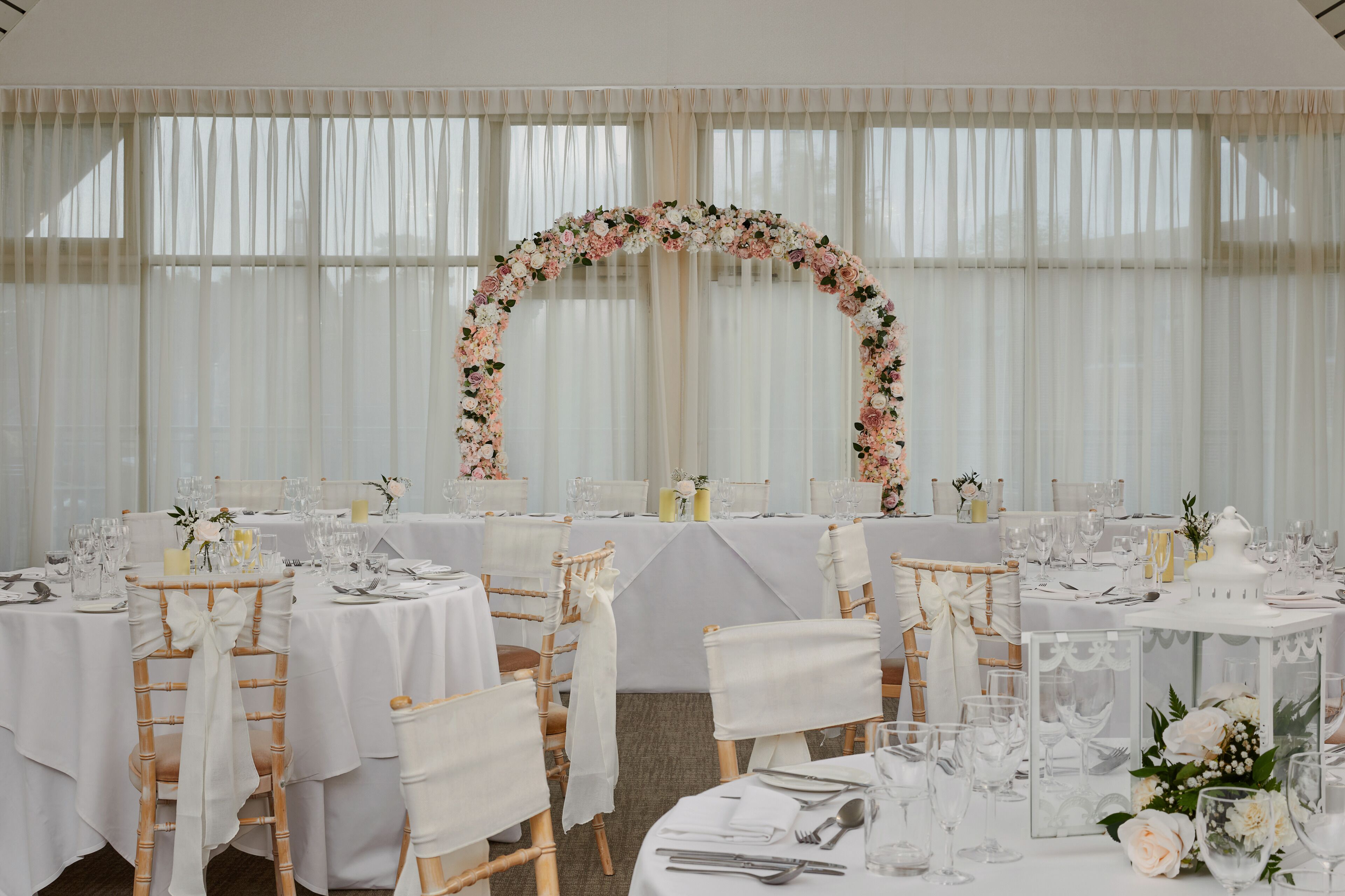 A banquet hall with round tables set for a formal event, featuring white tablecloths, floral centerpieces, and neatly arranged tableware.