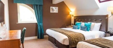 A hotel room with a bed, a desk, and a window with curtains.