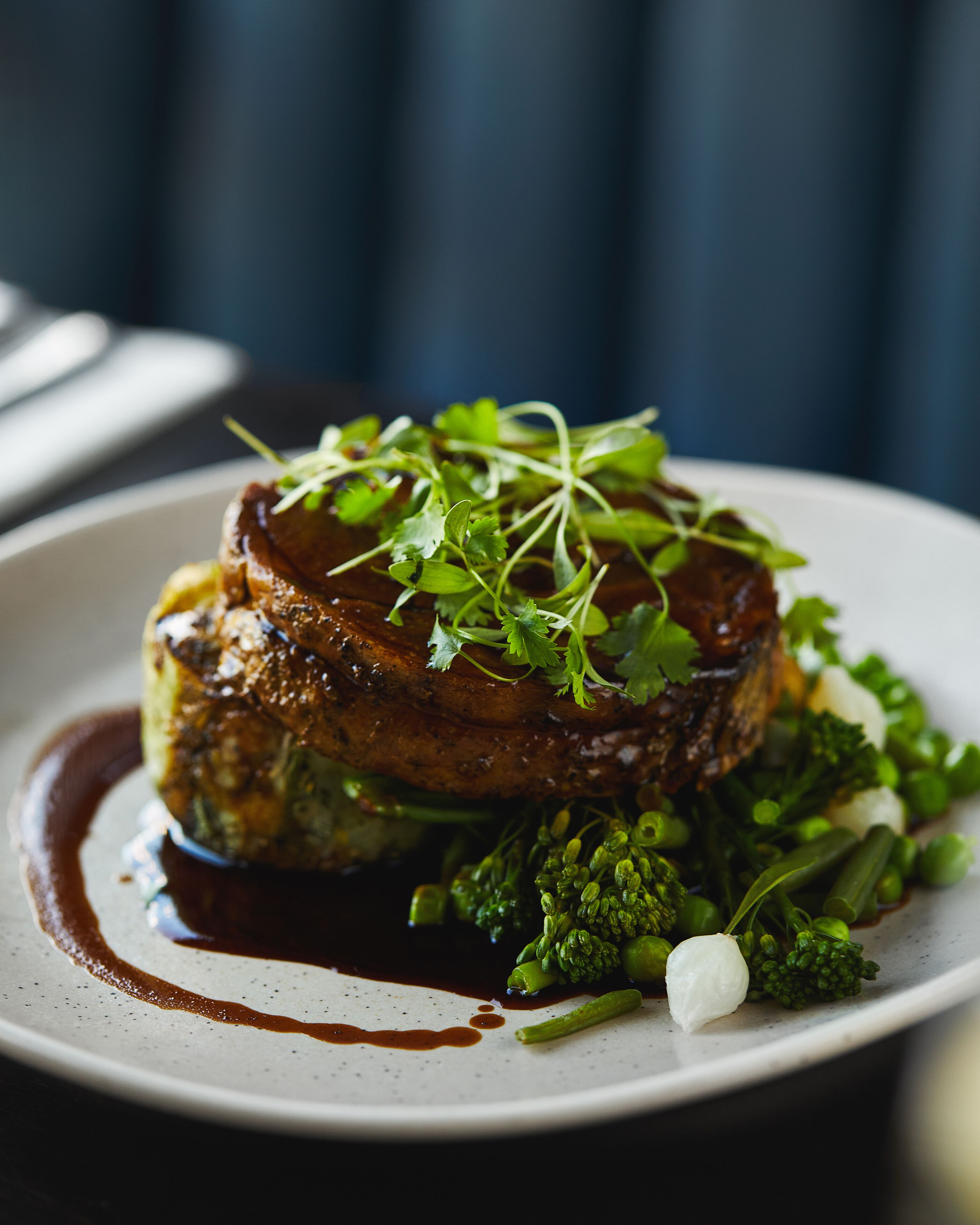 Une assiette de nourriture comprenant un steak, des légumes verts et une sauce.