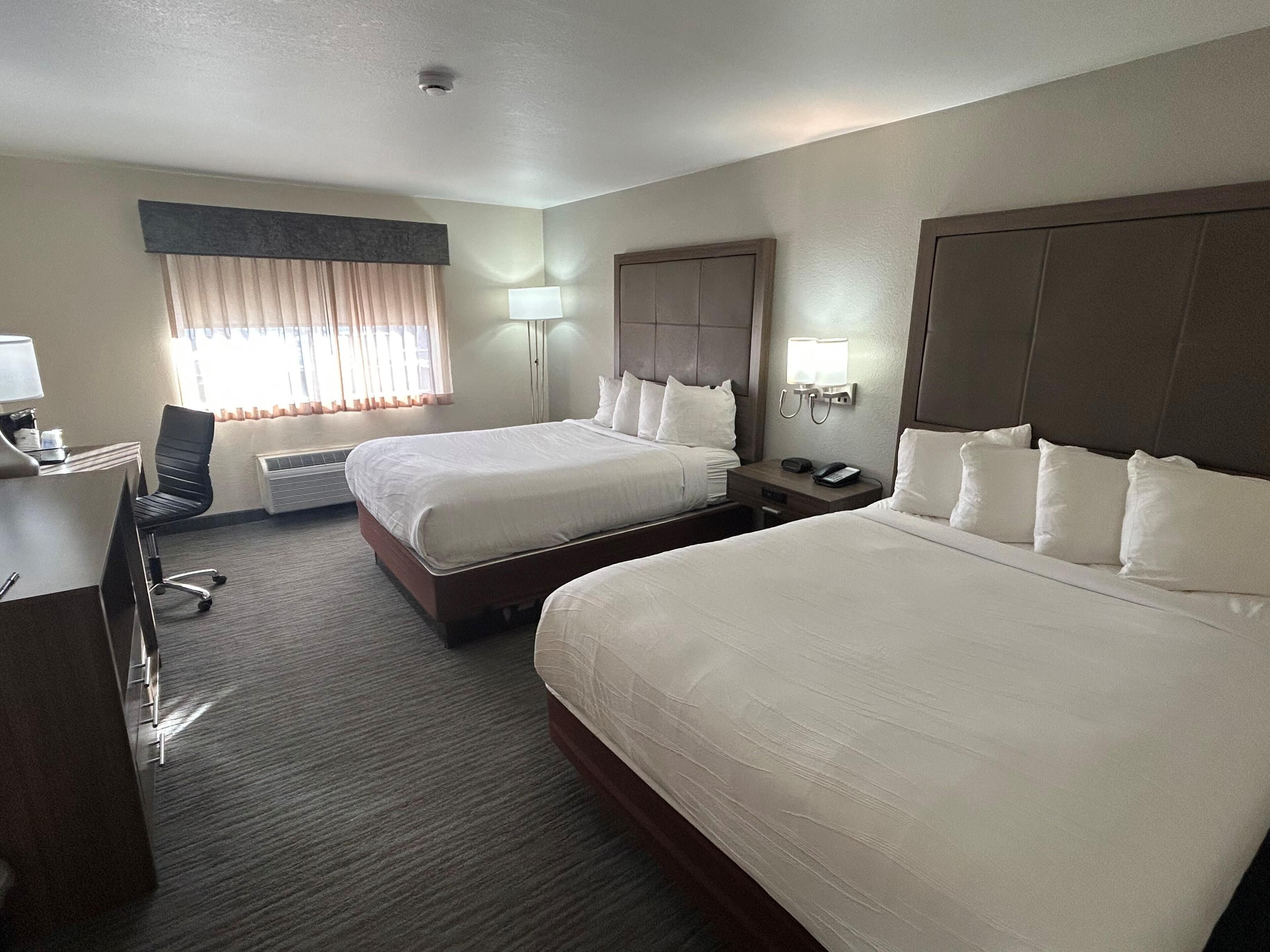 A hotel room with two beds, a desk, a chair, a lamp, and a telephone.