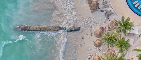 An aerial view of a beach with a swimming pool, palm trees, and lounge chairs.