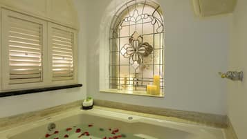 Une salle de bain avec une baignoire, une fenêtre ornée de vitraux et une étagère murale décorée de bougies.