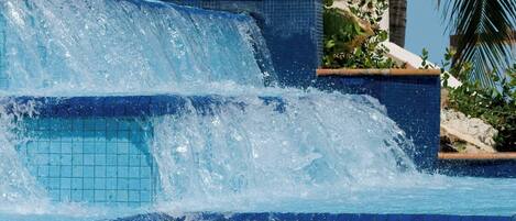 A pool with a cascading waterfall feature surrounded by palm trees.