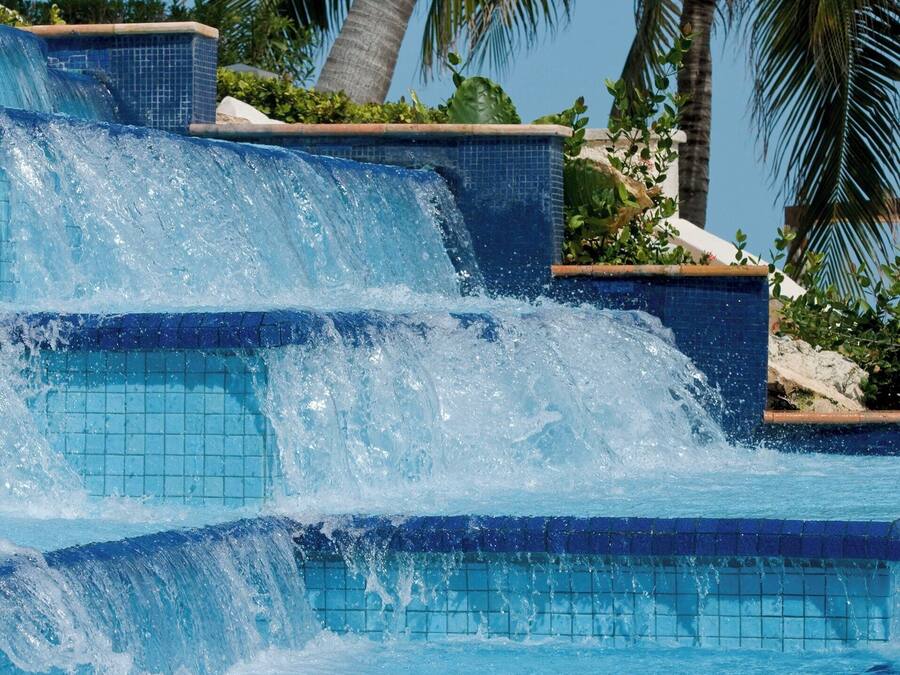 Una piscina con una cascada rodeada de palmeras.