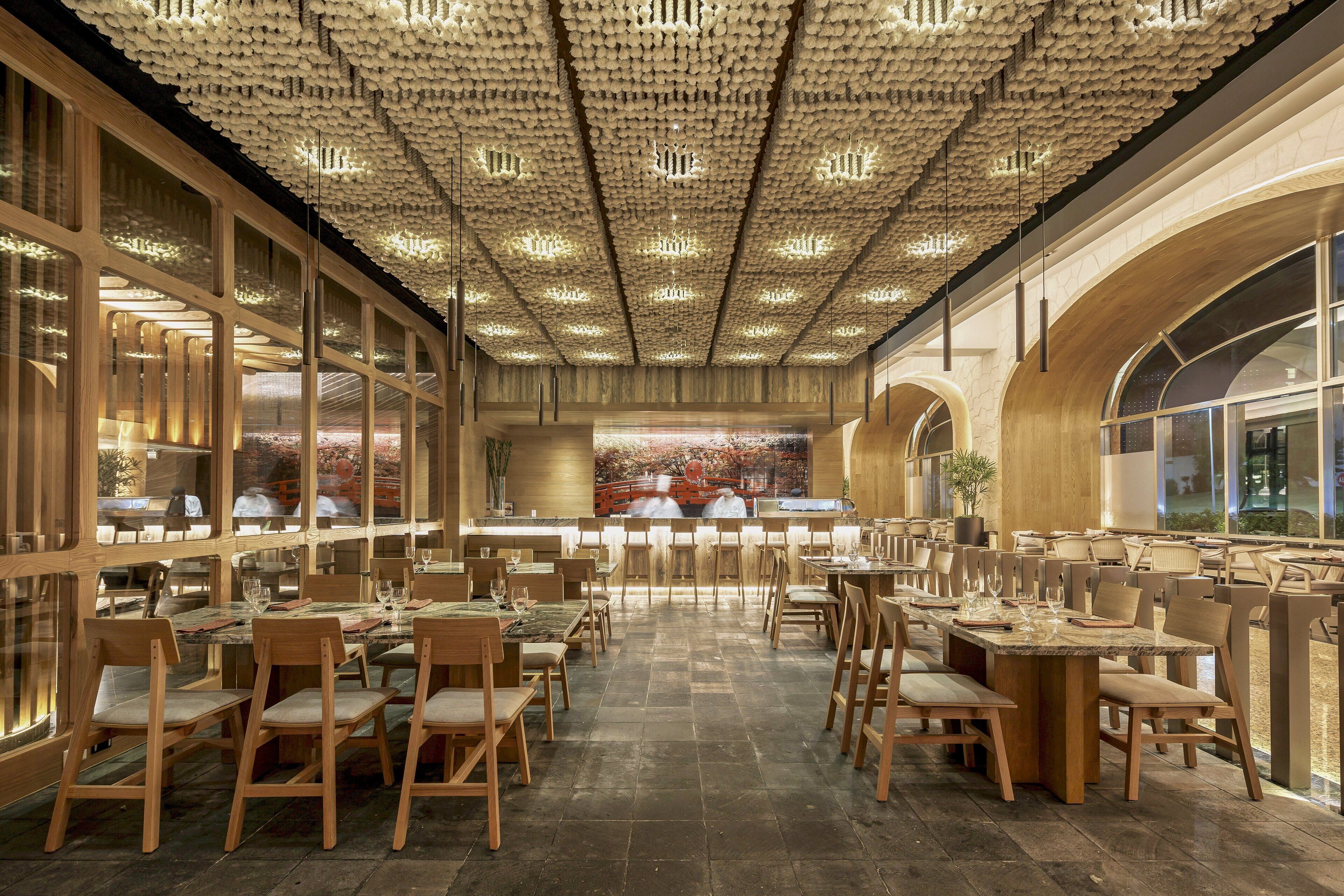 A spacious restaurant with wooden furniture, large windows, and a unique ceiling design.