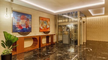 Un vestíbulo moderno con mostrador de recepción, obras de arte y un ascensor de cristal.