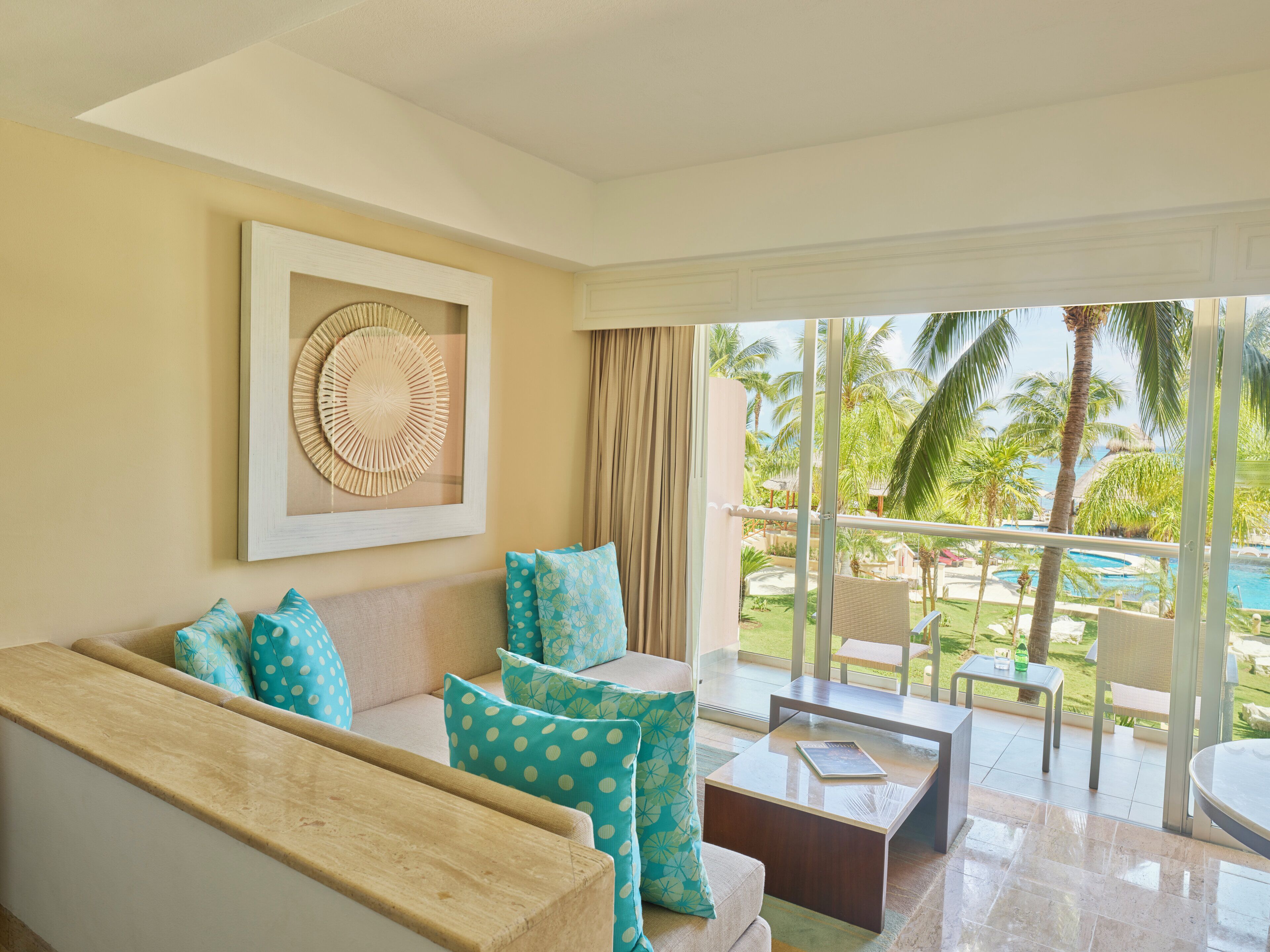 A modern living room with a sofa, coffee table, and a large window overlooking a pool and palm trees.