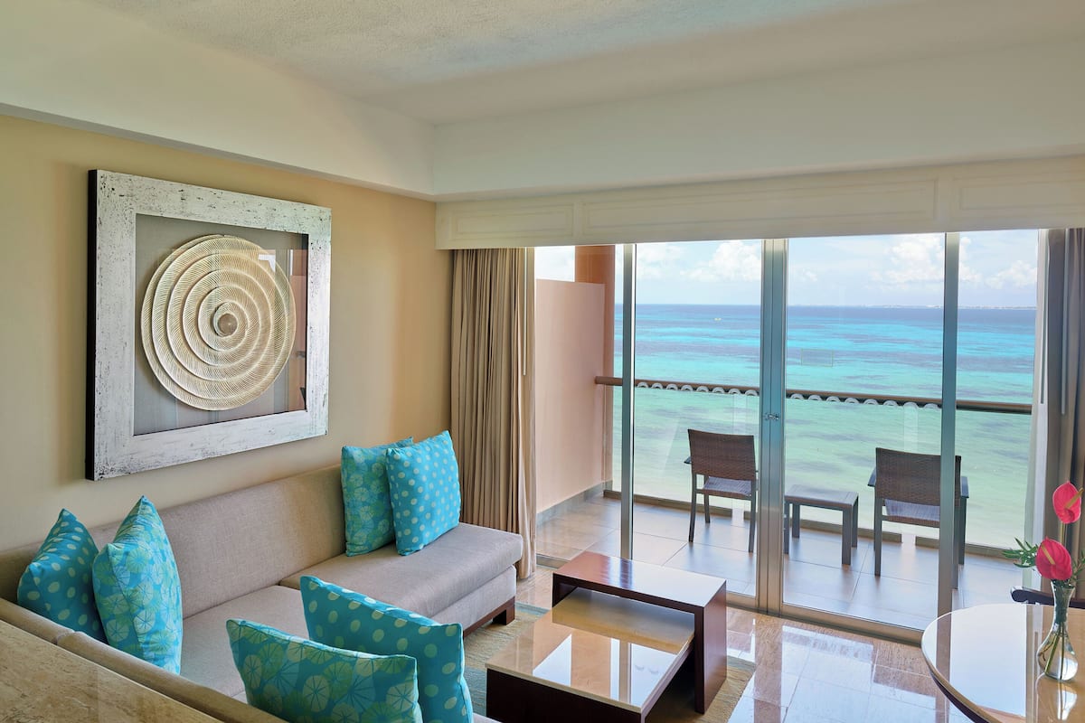 A balcony with a view of the ocean, a sofa with patterned cushions, and a table with a vase of flowers.