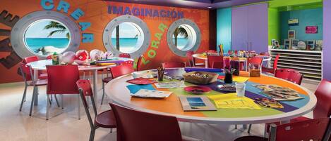 A colorful room with round windows, red chairs, and various art supplies on a table.