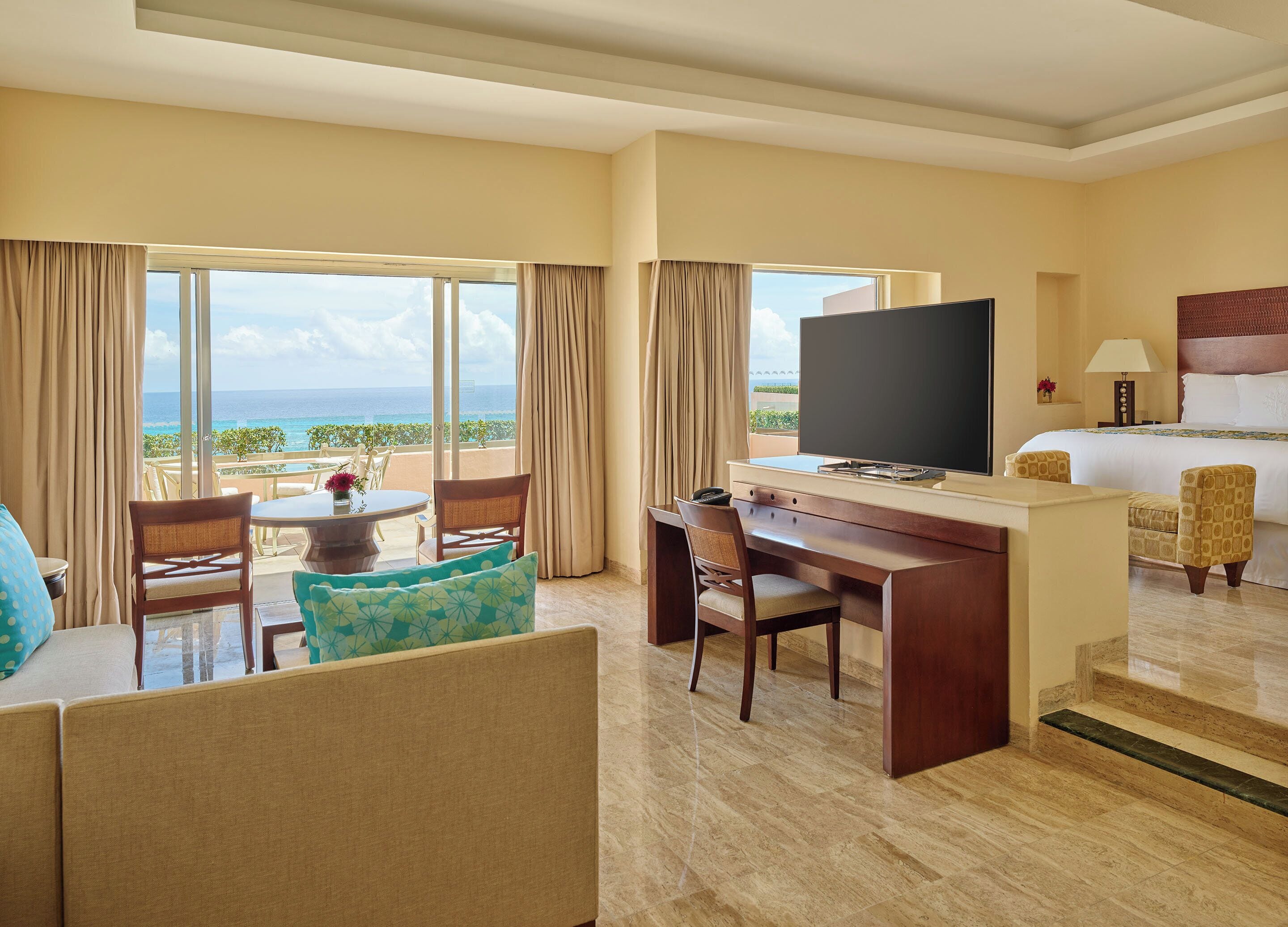 A hotel room with a bed, a desk, a television, and a view of the ocean.