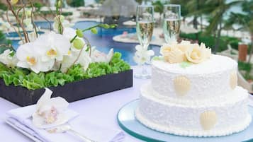 Un gâteau blanc à deux étages, décoré de motifs en forme de coquillages, posé sur un présentoir à gâteaux en verre.