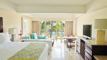 A hotel room with a large bed, a desk, a television, and a balcony with a view of palm trees.
