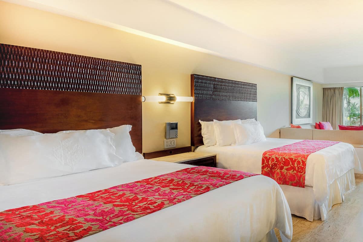 A hotel room with two beds, a desk, a chair, and a view of the outdoors.