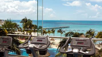 A treadmill with a digital display, positioned near a window overlooking a beach with palm trees and a pier.