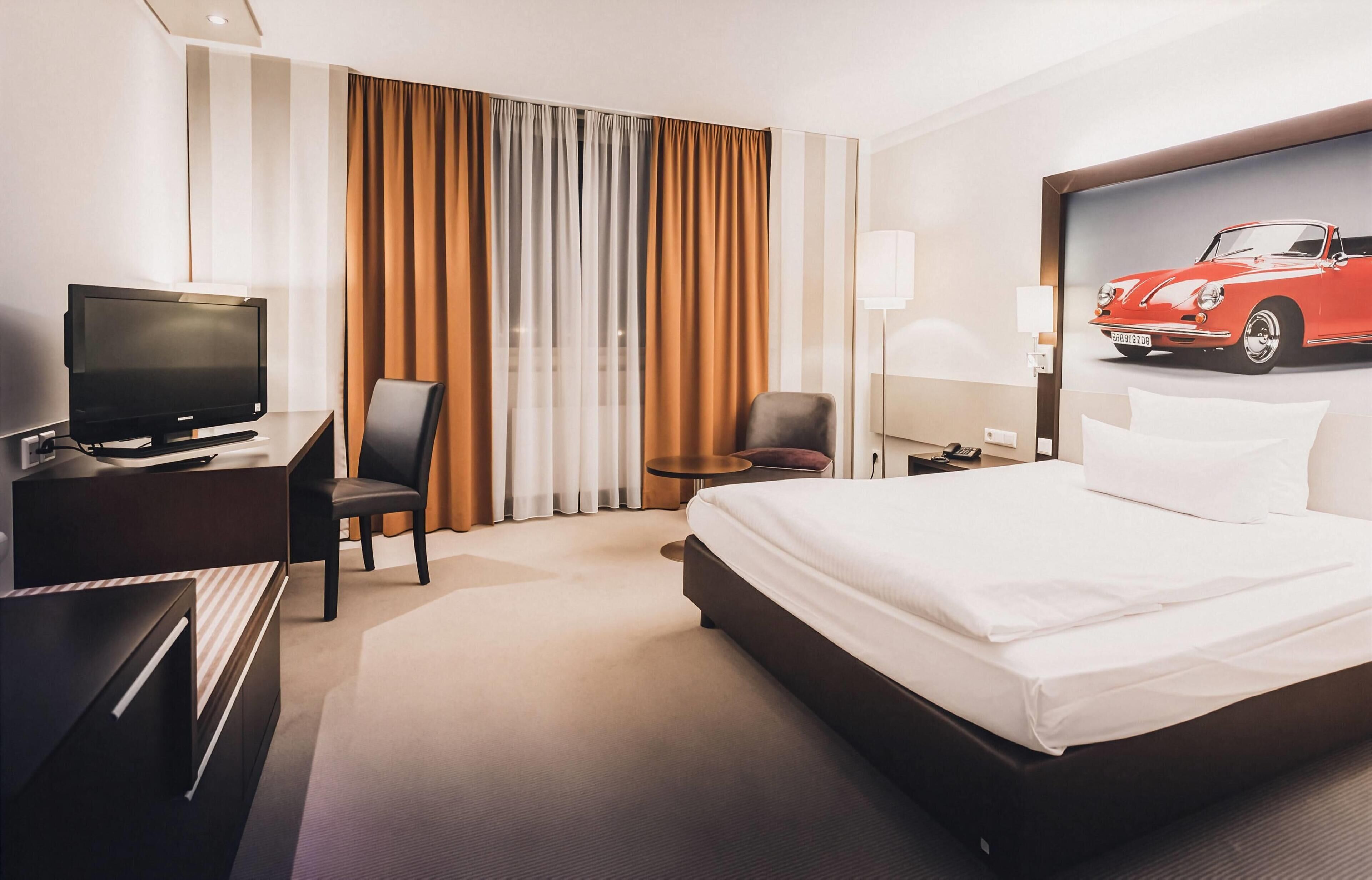 A hotel room with a bed, a desk with a television, a chair, a lamp, and a wall-mounted phone.