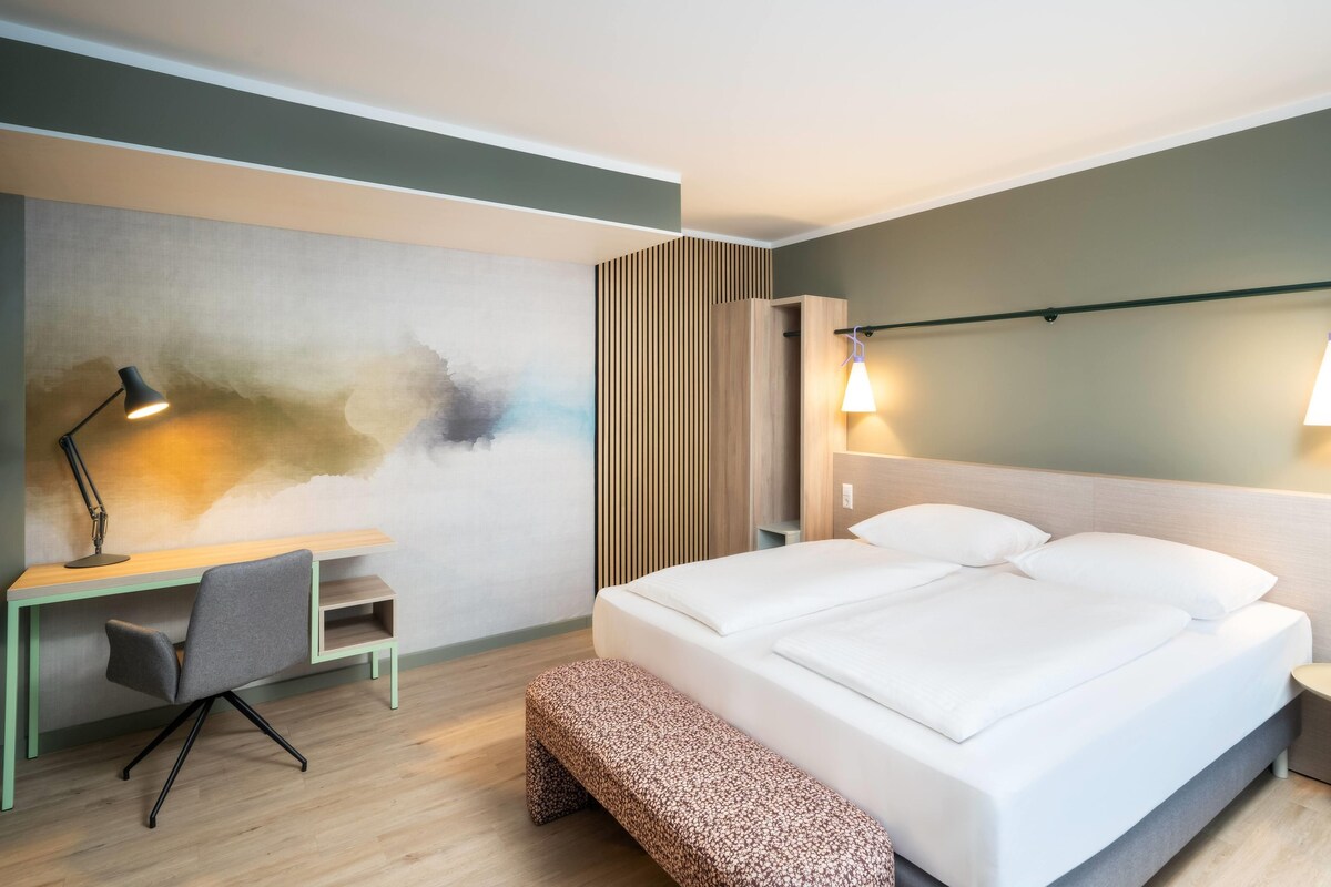 Ein Hotelzimmer mit Bett, Nachttisch, Schreibtisch mit Stuhl und einer Wand mit Strukturmuster.