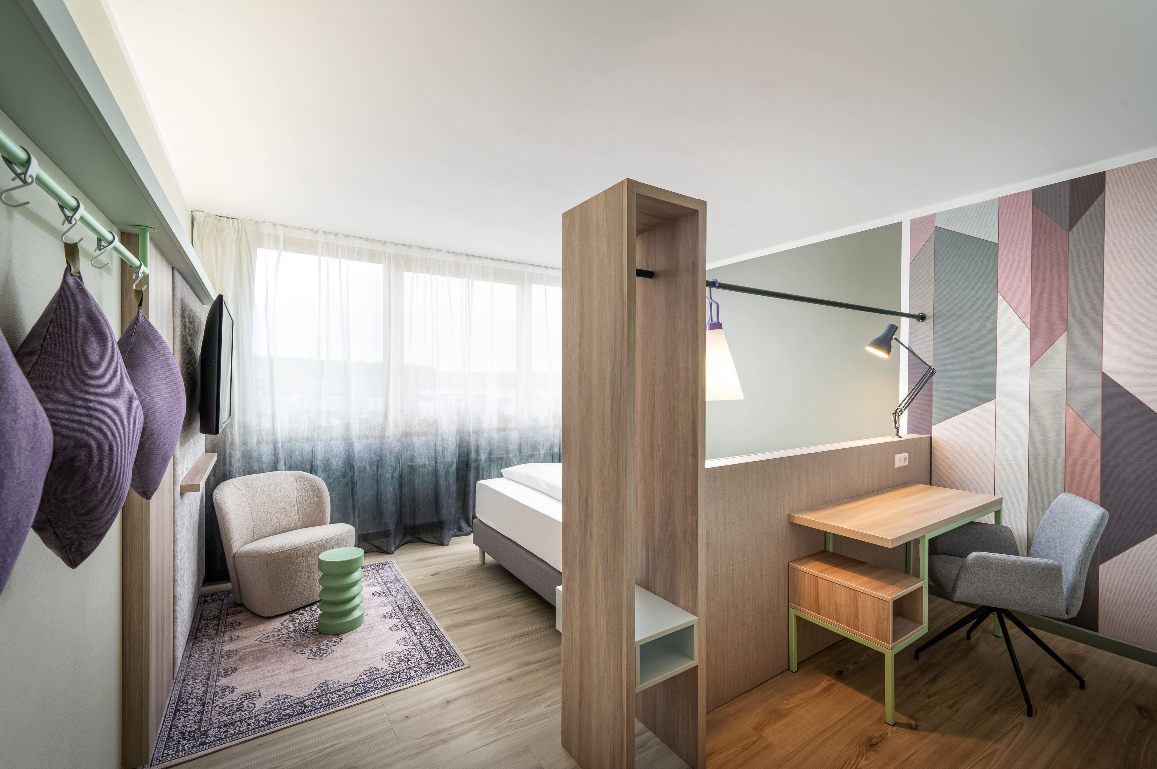 A modern bedroom with a bed, a desk, a chair, and a wardrobe.