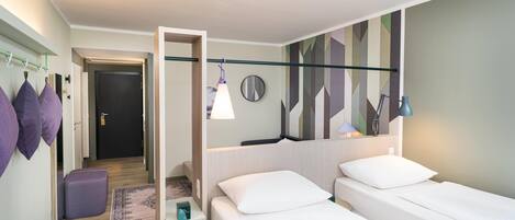 A hotel room with a bed, a bedside table, a mirror, a hanging light, and a wall with a geometric pattern.