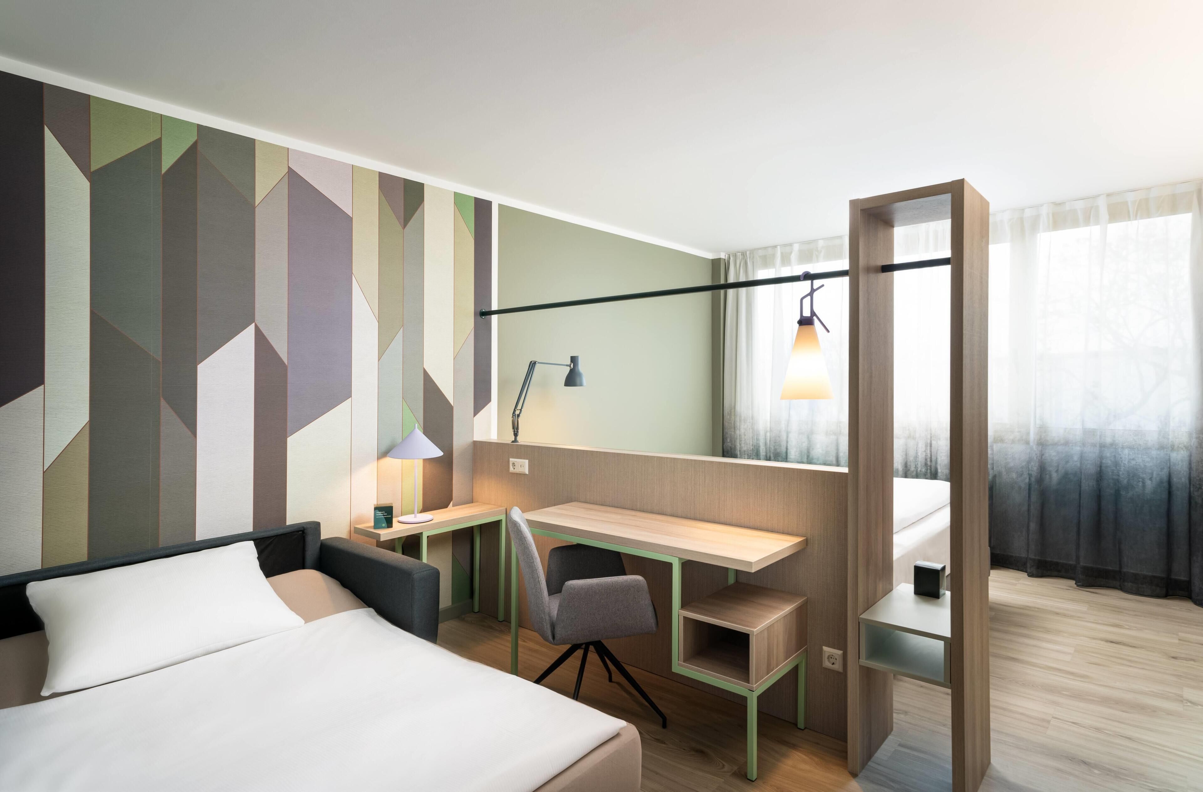 Een hotelkamer met een bed, een bureau, een stoel, een lamp en een raam met gordijnen.