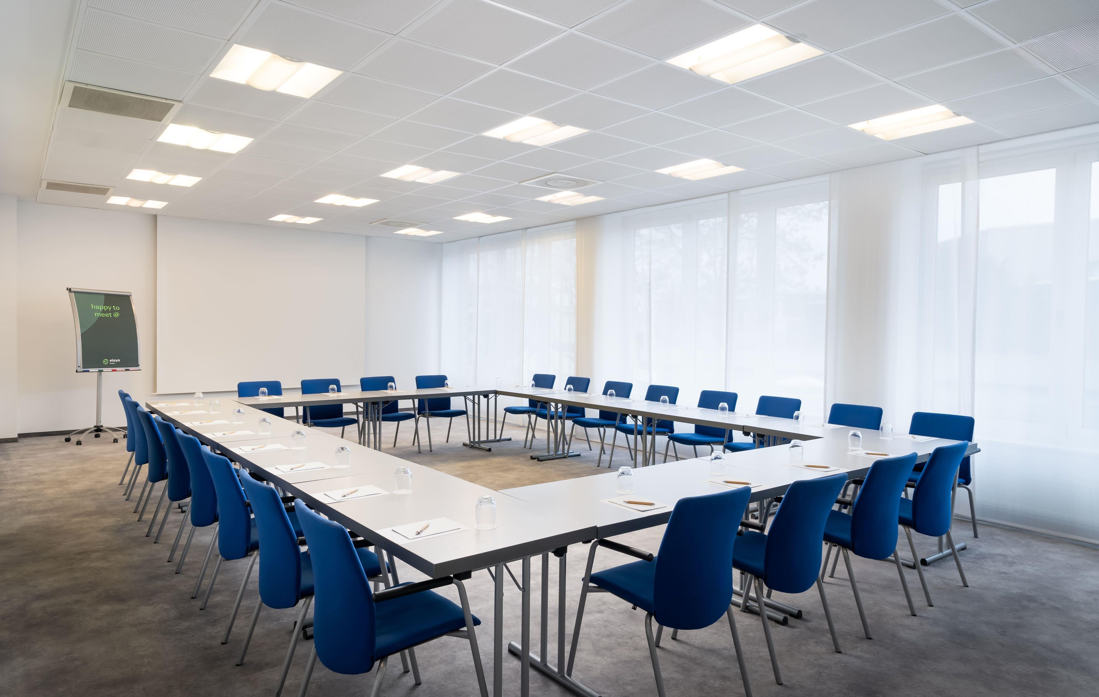A conference room with a long table, blue chairs, and a projector screen.