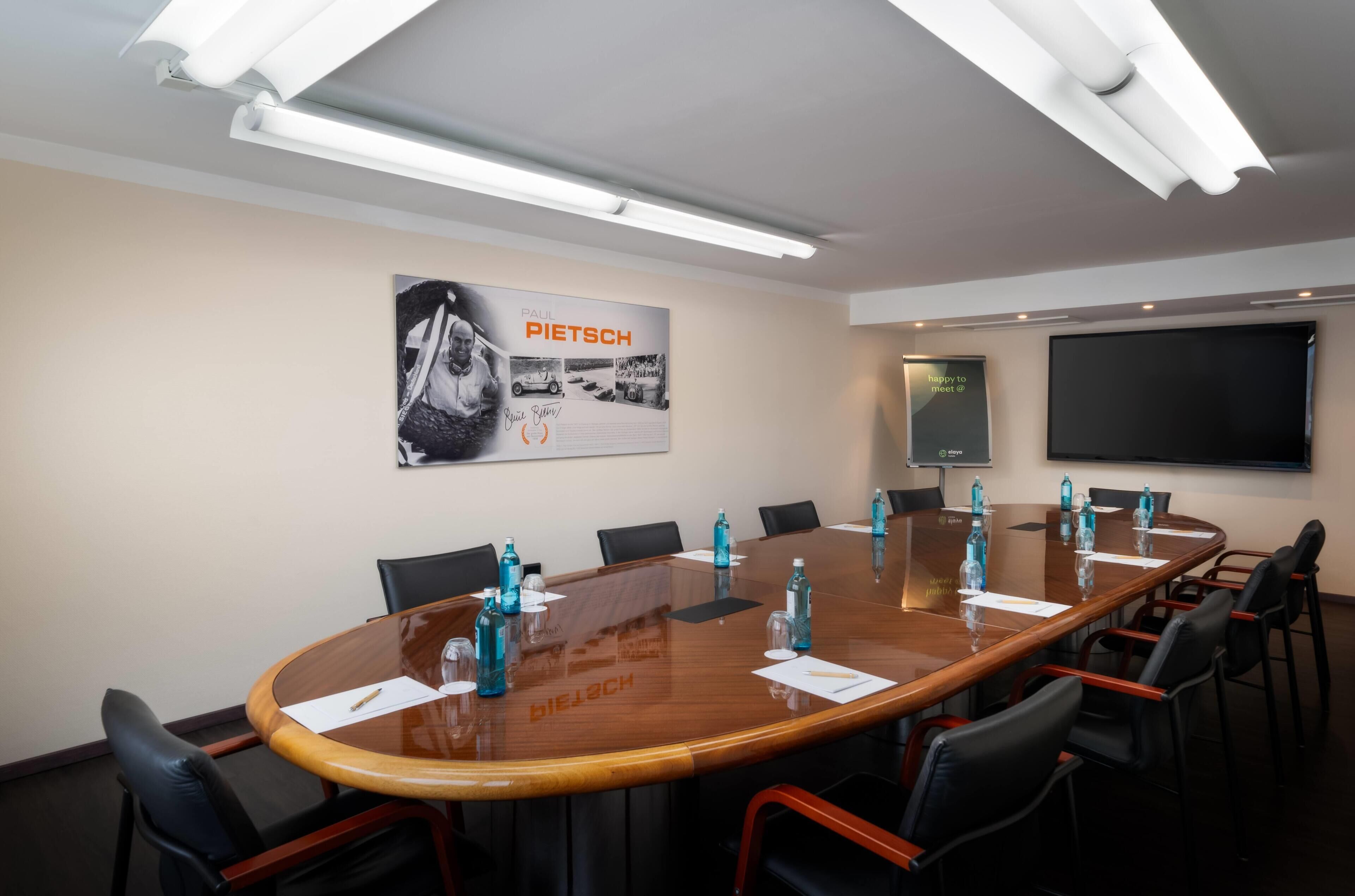 A conference room with a large oval table, black chairs, and a poster on the wall.