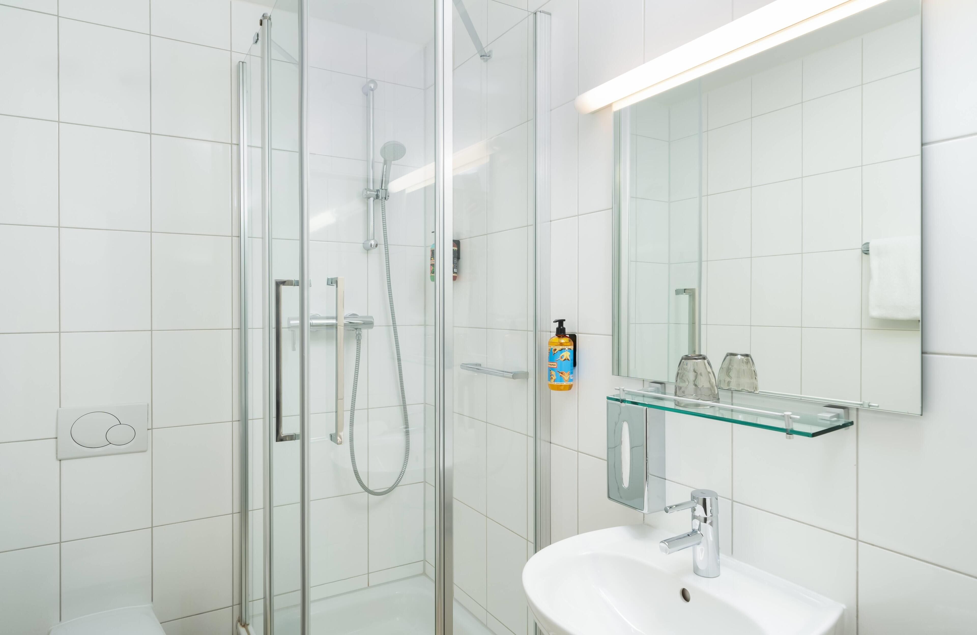 A modern bathroom with a glass shower enclosure, a white sink, and a glass shelf with toiletries.