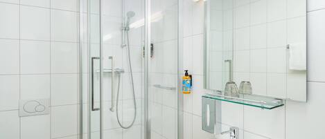 A modern bathroom with a glass shower enclosure, a white sink, and a glass shelf with toiletries.