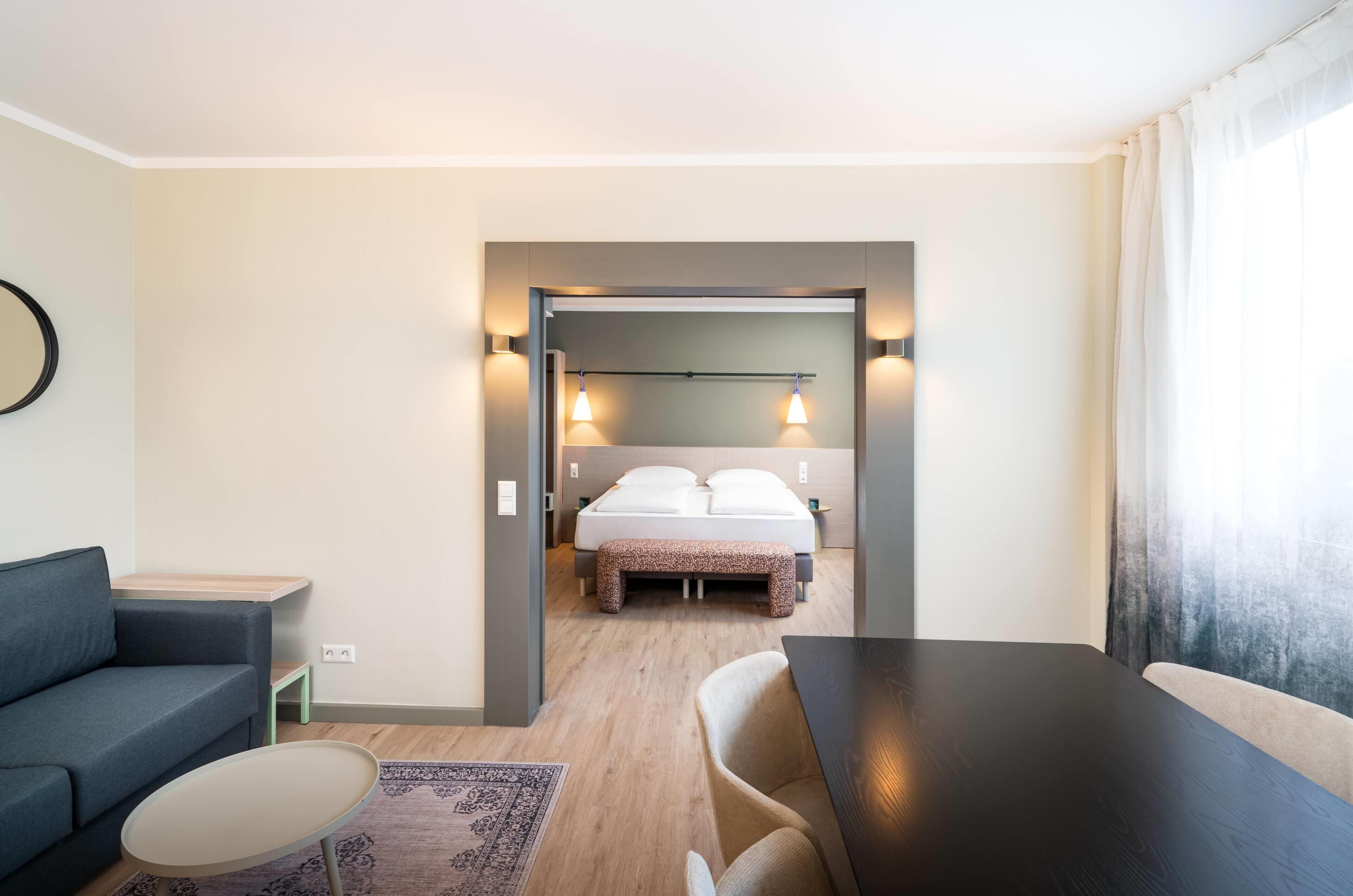 Habitació d'hotel moderna amb un llit, un sofà, una taula de dinar i una taula auxiliar.