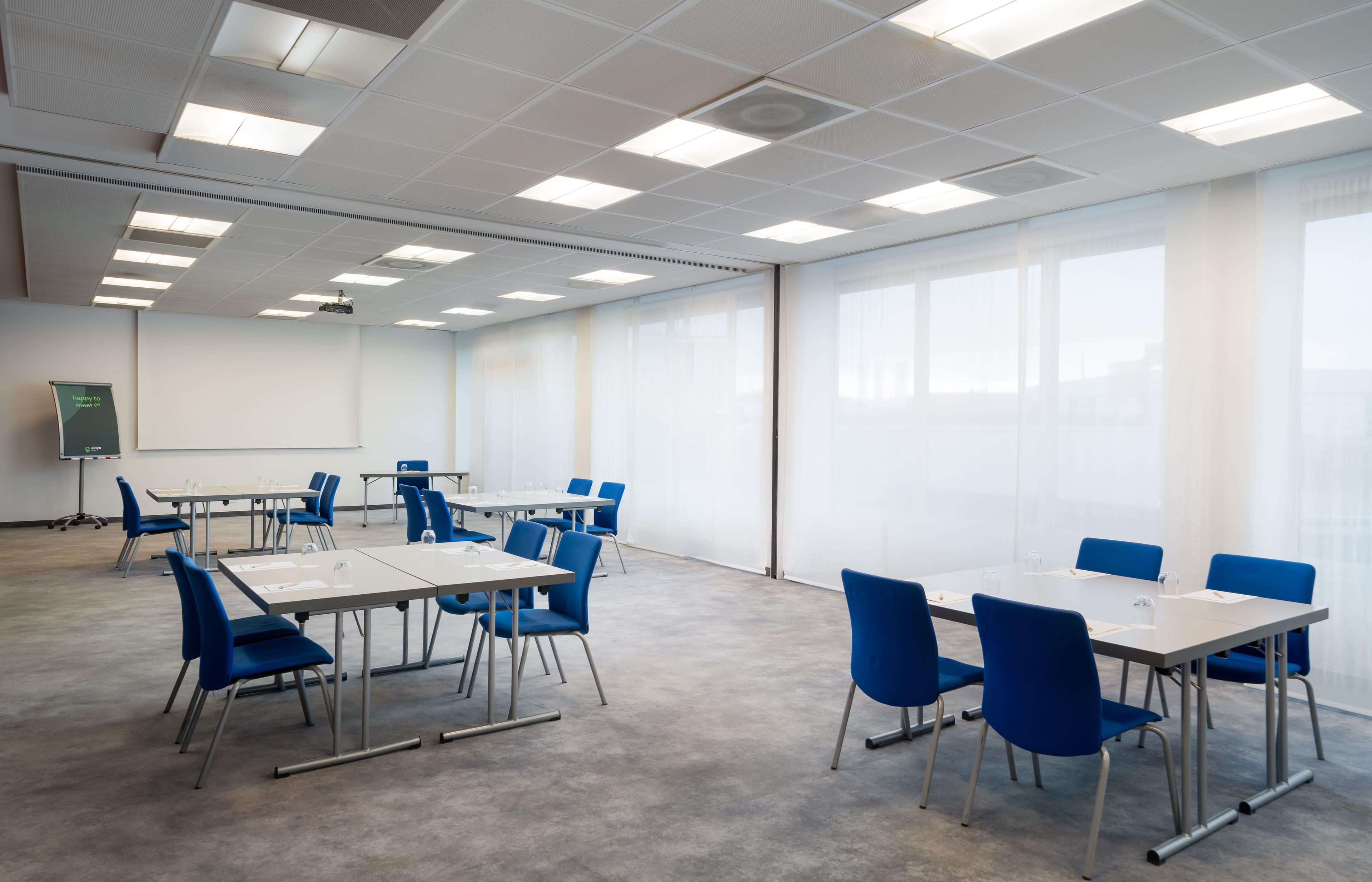 A conference room with tables and chairs, a projector screen, and large windows.
