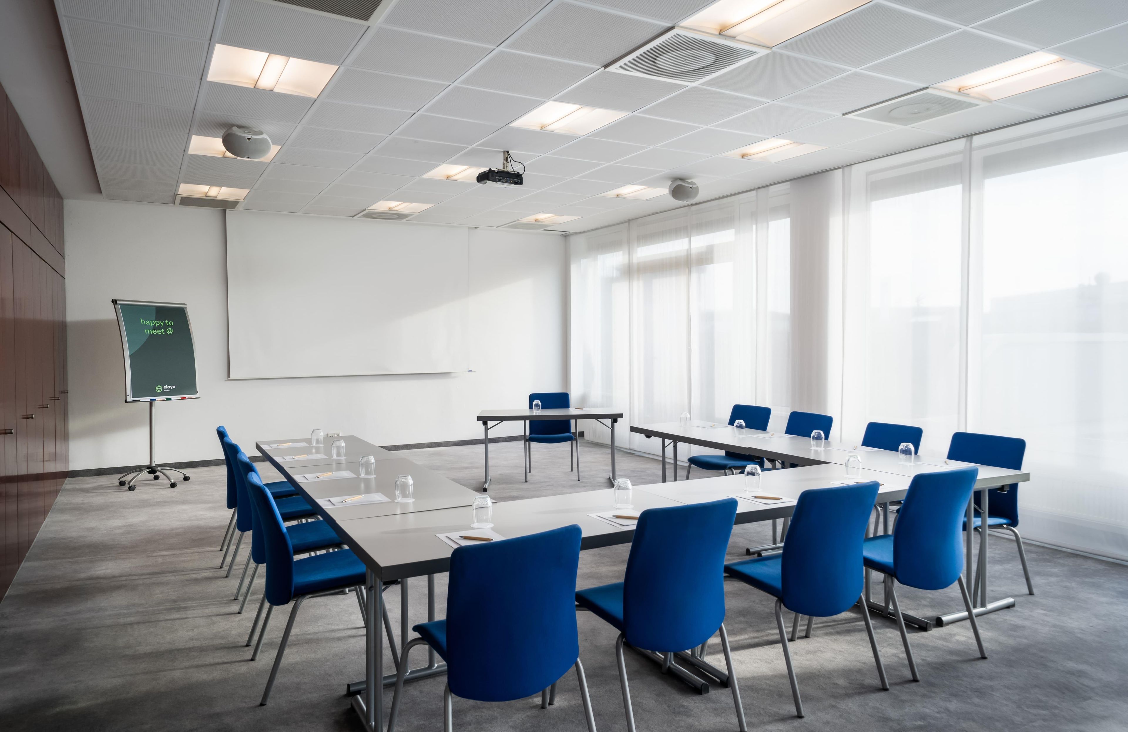 Une salle de conférence équipée d’une grande table, de chaises bleues, d’un tableau blanc et d’un projecteur.