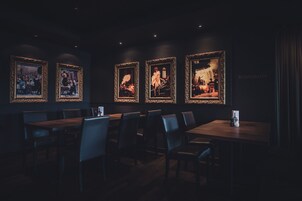 Un restaurante tenuemente iluminado con obras de arte enmarcadas en las paredes y mesas y sillas de madera.