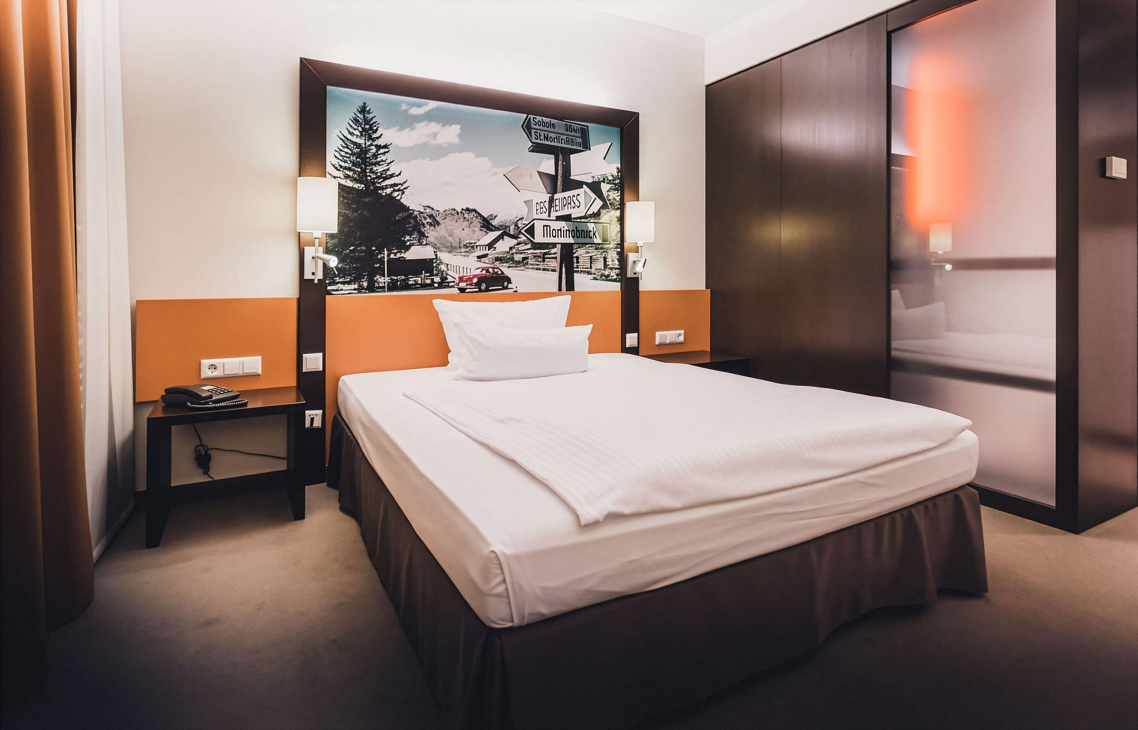 Una habitación de hotel con una cama, una mesita de noche, una lámpara y un letrero en la pared.