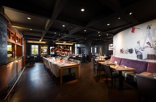 Un interior de restaurante con mesas comunes largas, cabinas individuales y una zona de bar.