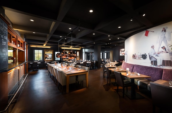 Un interior de restaurante con mesas comunes largas, cabinas individuales y una zona de bar.