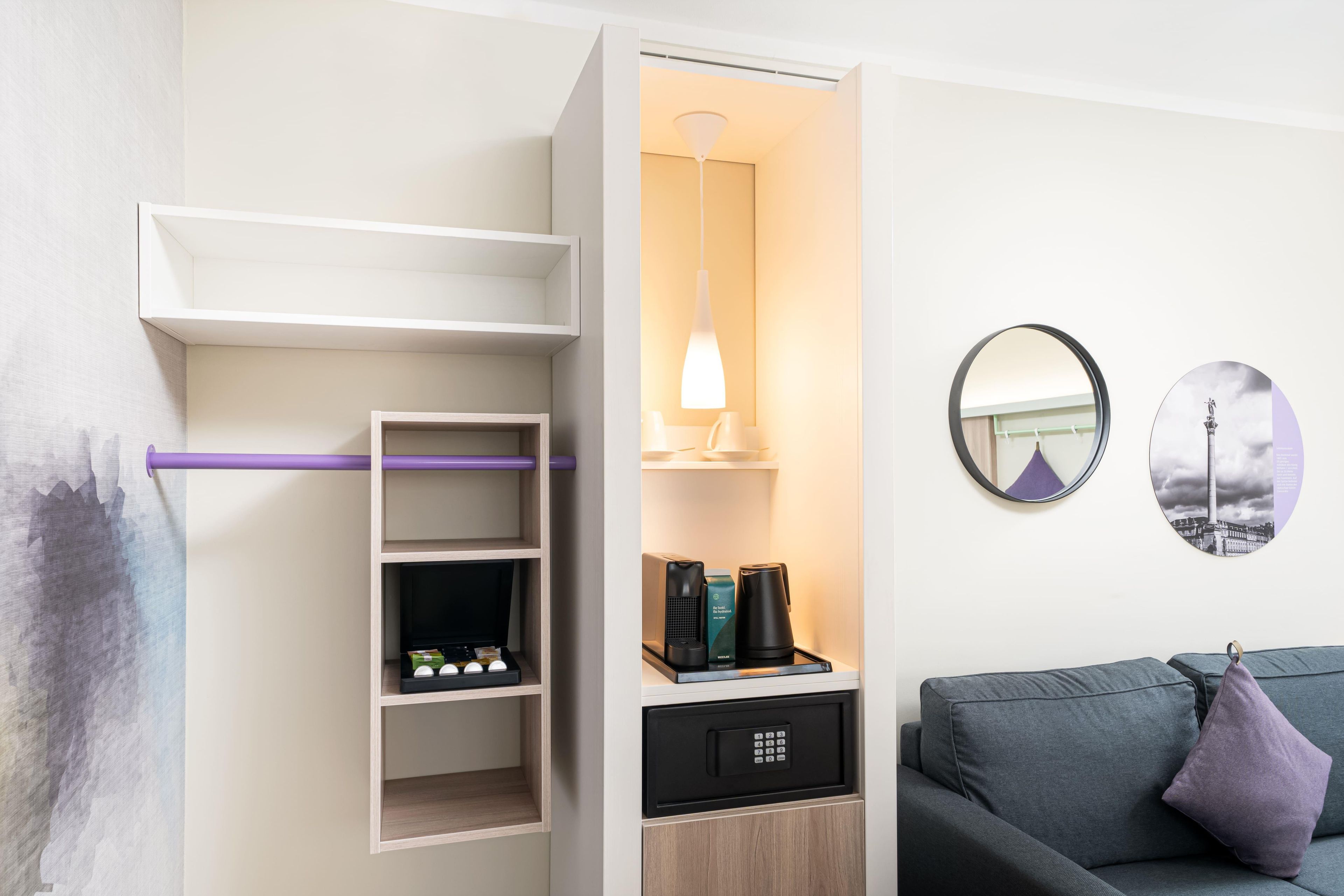 A modern room with a built-in wardrobe, a coffee machine, and a wall-mounted mirror.
