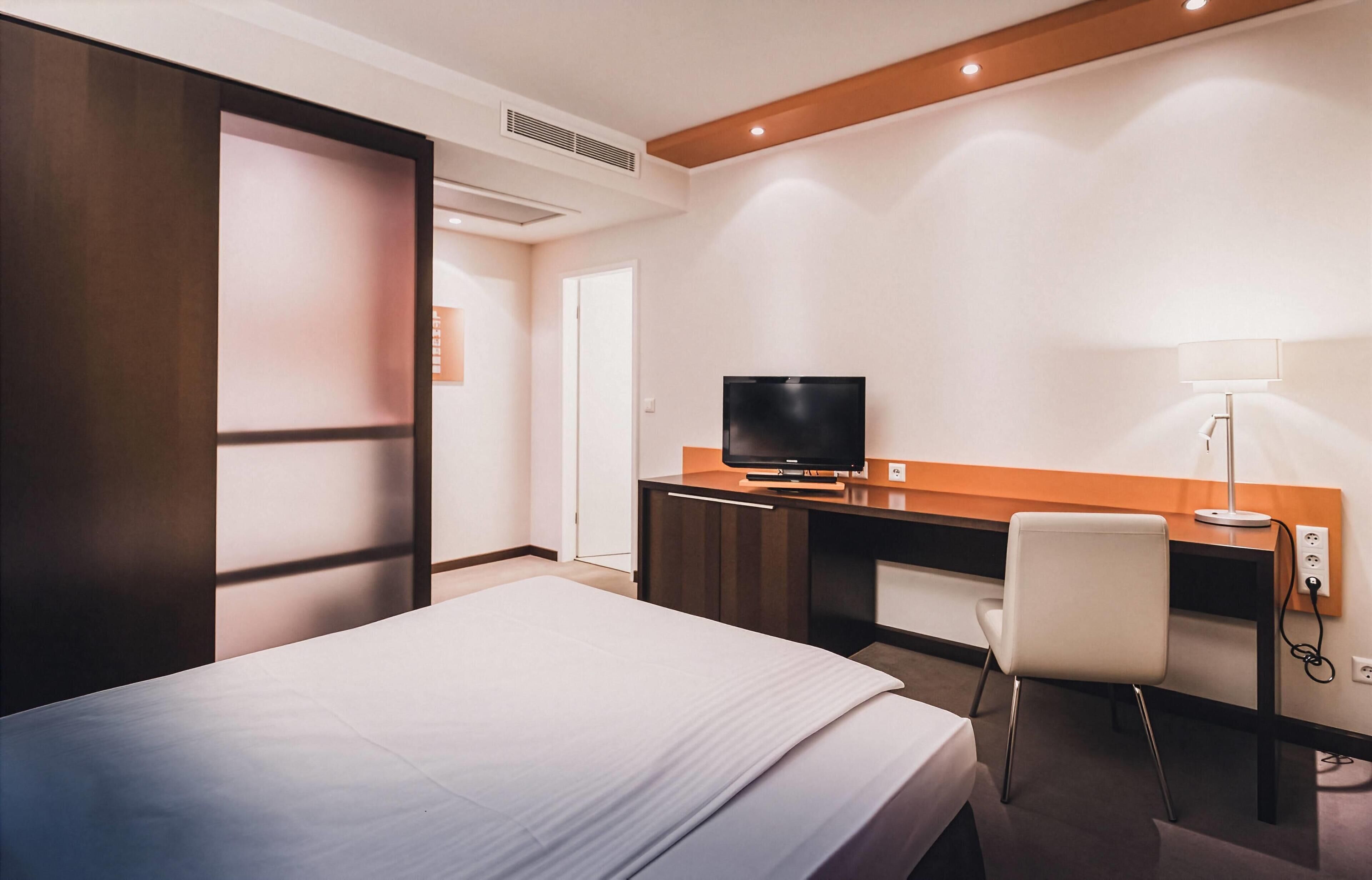 Une chambre d’hôtel comprenant un lit, un bureau avec une télévision, une chaise et une lampe.