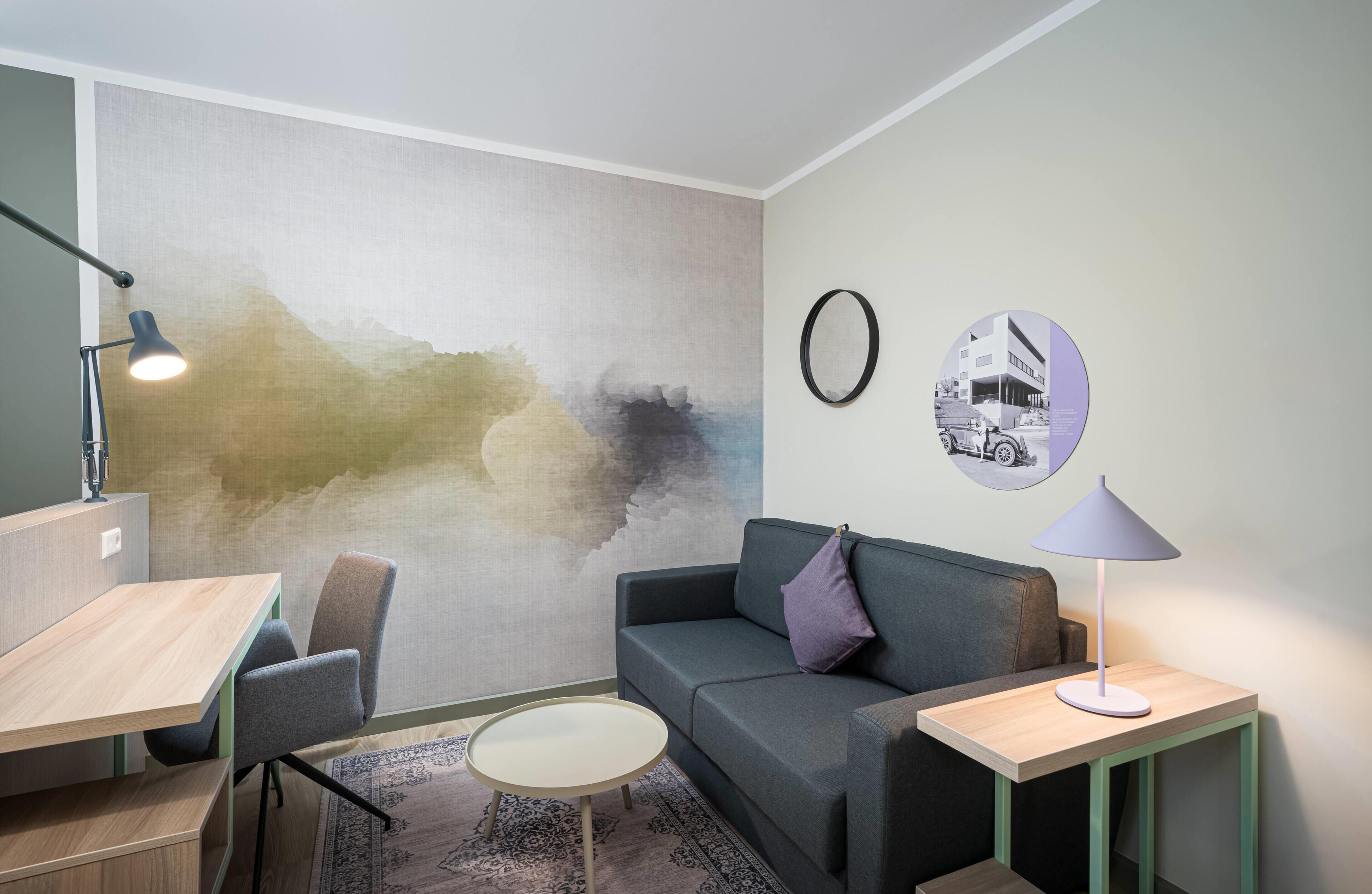 A modern living room with a grey sofa, a small round table, a desk, and a lamp.