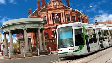 A tram with the number 3027 approaching a building with a classical facade and a circular entrance.